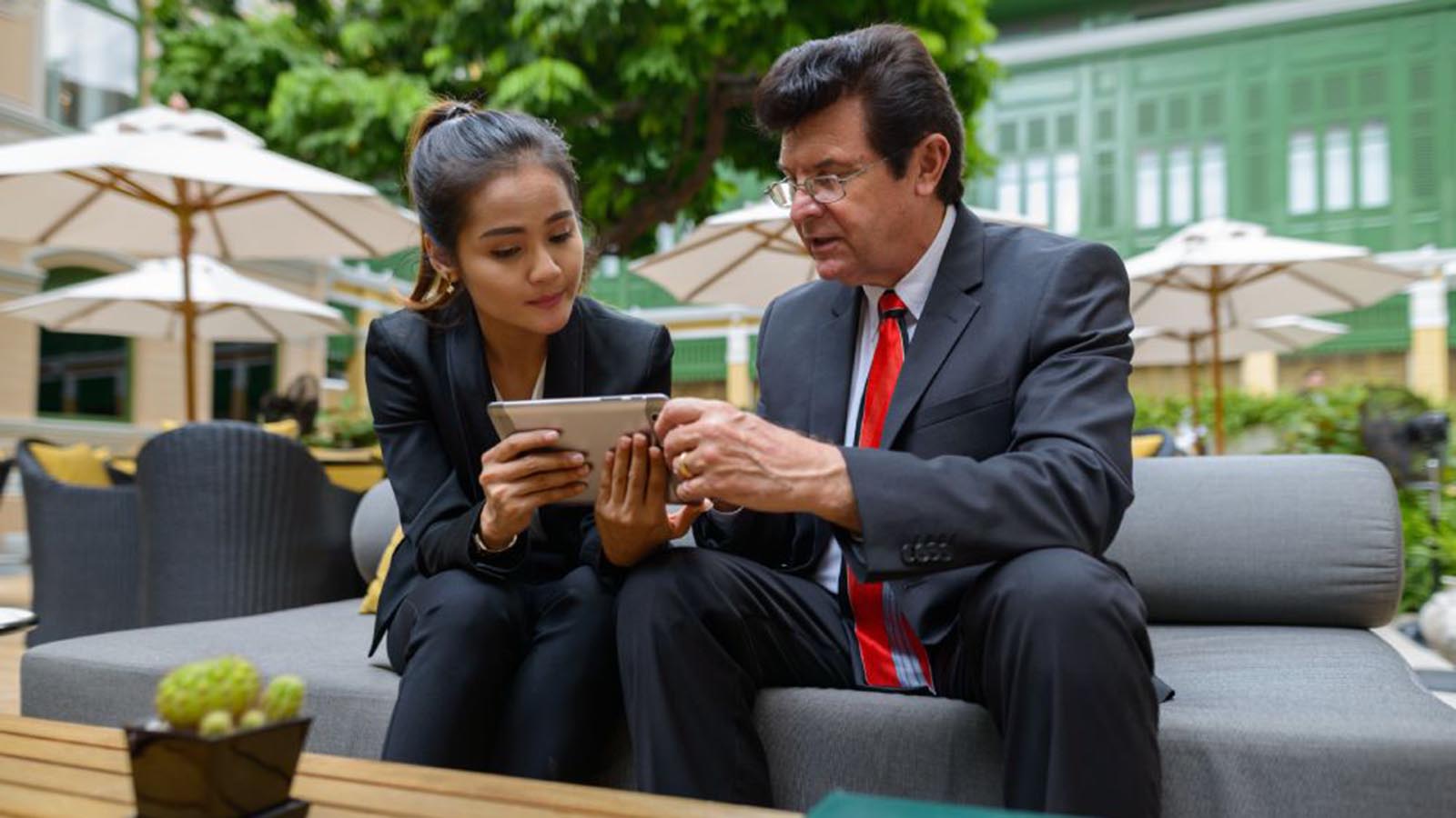 Mature businessman and young Asian businesswoman using digital tablet together